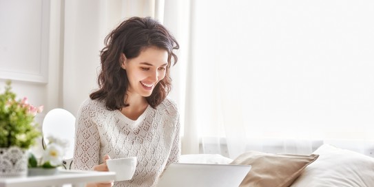 Frau schaut lächeld auf ihren Laptopbildschirm