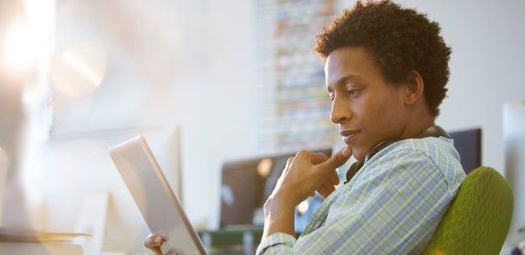 Ein Mann schaut nachdenklich auf sein Tablet und hält sich das Kinn