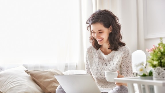 Frau schaut lächelnd auf Ihren Laptop-Bildschirm