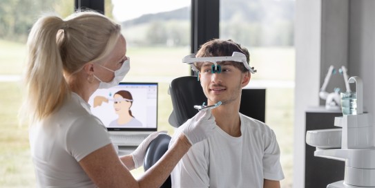 Zahnärztin justiert ein Gesichtsbogen-Messgerät bei einem jungen Patienten in moderner Praxisumgebung.